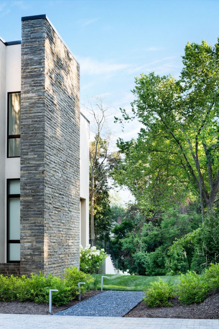 A curved drive, hornbeam hedge, allée of birches, and wildflower meadow together create privacy and lovely elements of surprise on the approach to this new house, which was designed for entertaining. Luxurious, but low-maintenance native and adaptive plantings are integrated into the overall landscape plan to balance the considerable hardscaping and define the lawns. At the front of the house, a massive parking court with subtly striped paving and an elegant retaining wall create a distinctive outdoor room. Guests have a variety of gathering spaces at the rear of the house that include upper and lower terraces for seating and dining, a putting green, and pool and pool deck. A large rain garden in the lower slope completes the program requirements by absorbing drainage and recharging the aquifer.