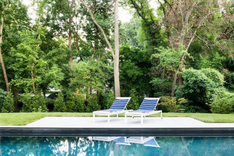 A curved drive, hornbeam hedge, allée of birches, and wildflower meadow together create privacy and lovely elements of surprise on the approach to this new house, which was designed for entertaining. Luxurious, but low-maintenance native and adaptive plantings are integrated into the overall landscape plan to balance the considerable hardscaping and define the lawns. At the front of the house, a massive parking court with subtly striped paving and an elegant retaining wall create a distinctive outdoor room. Guests have a variety of gathering spaces at the rear of the house that include upper and lower terraces for seating and dining, a putting green, and pool and pool deck. A large rain garden in the lower slope completes the program requirements by absorbing drainage and recharging the aquifer.