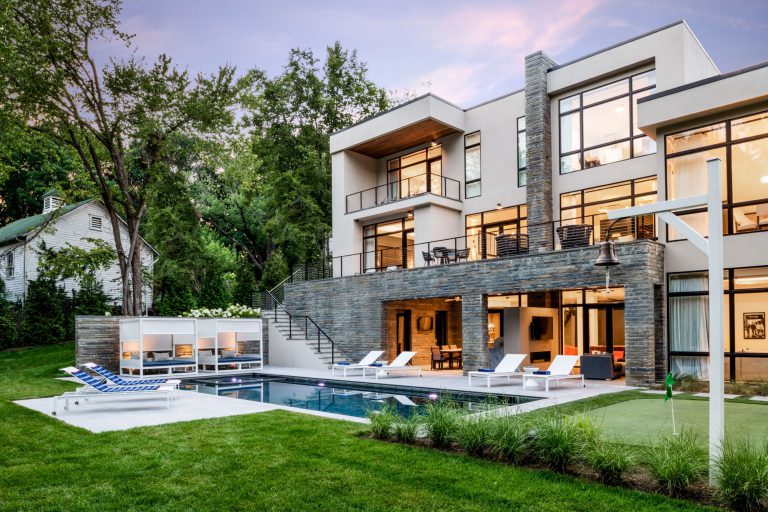 A curved drive, hornbeam hedge, allée of birches, and wildflower meadow together create privacy and lovely elements of surprise on the approach to this new house, which was designed for entertaining. Luxurious, but low-maintenance native and adaptive plantings are integrated into the overall landscape plan to balance the considerable hardscaping and define the lawns. At the front of the house, a massive parking court with subtly striped paving and an elegant retaining wall create a distinctive outdoor room. Guests have a variety of gathering spaces at the rear of the house that include upper and lower terraces for seating and dining, a putting green, and pool and pool deck. A large rain garden in the lower slope completes the program requirements by absorbing drainage and recharging the aquifer.