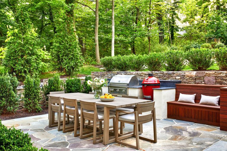 The integration of classical garden elements with a looser, but no less specific approach addresses the husband and wife’s different design sensibilities. The entry garden pairs formal shapes with low plantings and perennial flowers. At the rear, traditional dry stack retaining walls surrounding the entertaining area appear beautifully contemporary in their expression. Two patios—one for cooking and dining, the other for repose around a fireplace—are connected via a walkway of pavers surrounded by river stone, which in turn are bordered by traditional boxwood, boulders, ornamental grasses, and perennial flowers. To reinforce the inside/outside connection, an axial path of stone in running bond leads from the front door through the house to culminate in the back garden. Upon arriving at the terrace stair, the stone path gives way to an irregular pattern that defines the patio areas.