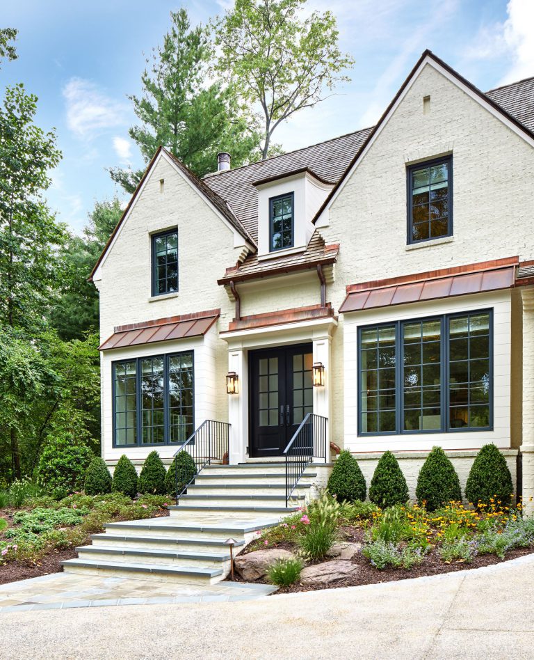 The integration of classical garden elements with a looser, but no less specific approach addresses the husband and wife’s different design sensibilities. The entry garden pairs formal shapes with low plantings and perennial flowers. At the rear, traditional dry stack retaining walls surrounding the entertaining area appear beautifully contemporary in their expression. Two patios—one for cooking and dining, the other for repose around a fireplace—are connected via a walkway of pavers surrounded by river stone, which in turn are bordered by traditional boxwood, boulders, ornamental grasses, and perennial flowers. To reinforce the inside/outside connection, an axial path of stone in running bond leads from the front door through the house to culminate in the back garden. Upon arriving at the terrace stair, the stone path gives way to an irregular pattern that defines the patio areas.