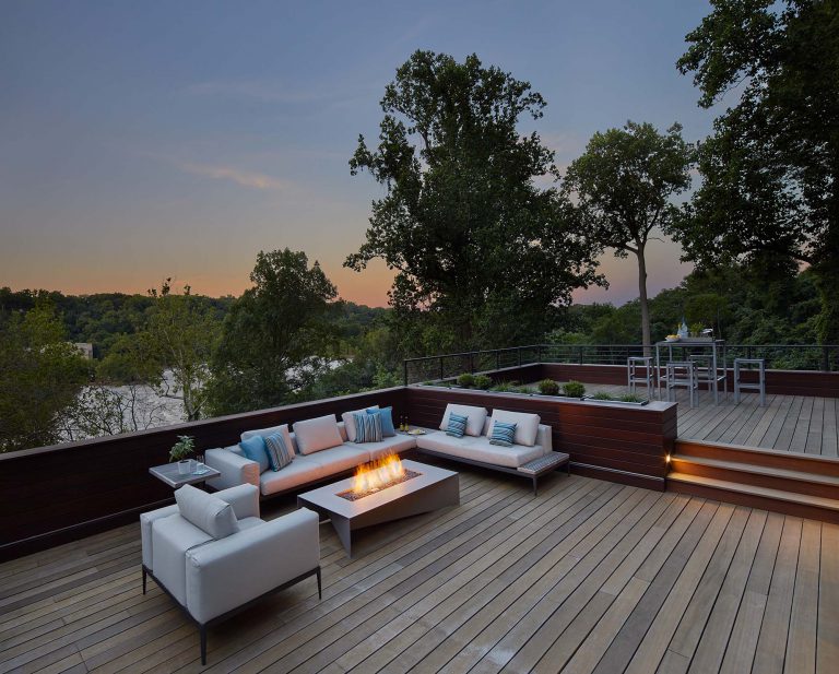 Cozy deck sitting area with burning fire at dusk overlooking lake, designed by Landscape Architect DC Joseph Richardson.