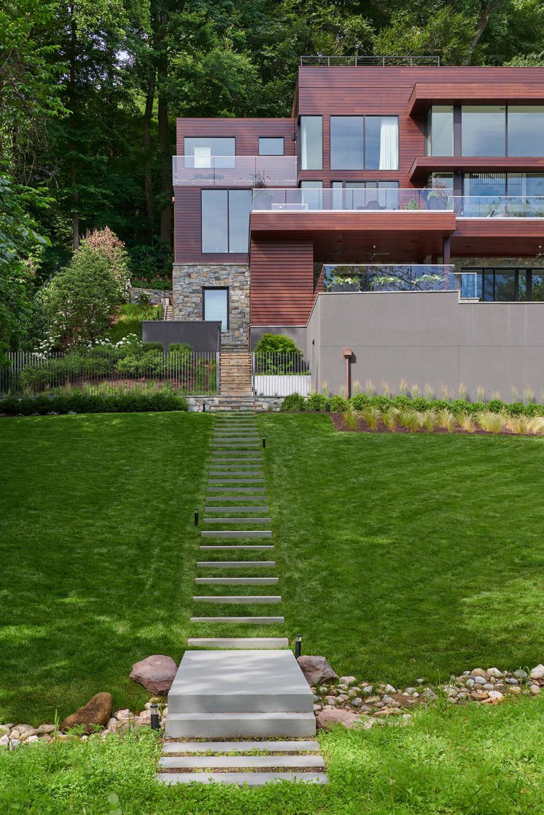 The masterplan for this unique property — a steeply sloping three-acre site and riverfront clearing — included stabilizing eroded creeks, restoring wetlands, and incorporating a massive rain garden to filter storm water flow from the parking court above and other properties further up the hill. The owners, a family with four dogs, also had requirements that included adequate parking for entertaining, a dedicated recreation space for the dogs, and a beautifully blended network of new plantings, hardscape, and sculpture to be seen from and complement the linear forms of their organic-modern home in the woods.
